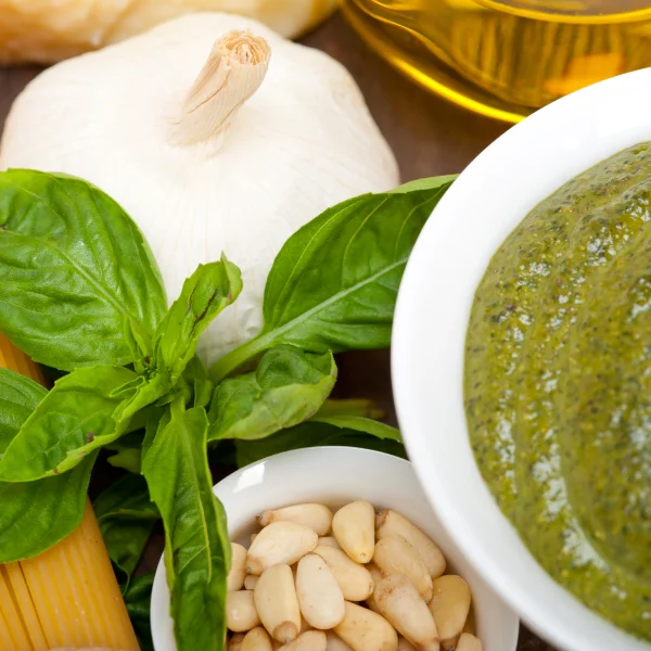 Un bol de pesto à côté d'un bol de pâtes et d'un bol d'ail, idéal pour une sauce à spaghetti savoureuse.