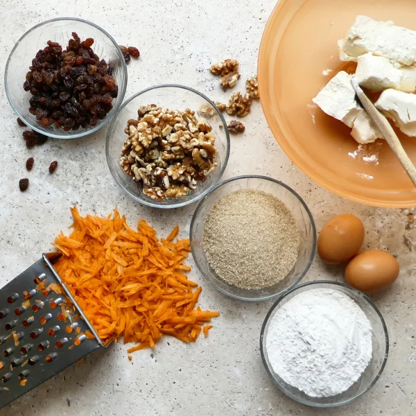 Ingrédients pour un gâteau aux carottes, incluant carottes, farine, sucre et épices, sur un plan de travail.