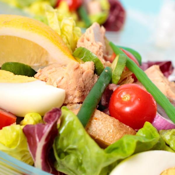 Gros plan d'une salade niçoise fraîche avec du thon, un œuf bouilli, des tomates cerises, des haricots verts et un quartier de citron.