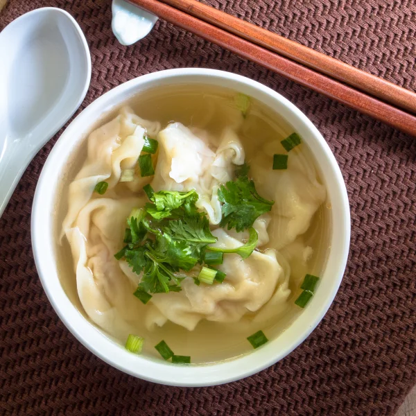 Soupe de raviolis chinois avec des baguettes, présentée comme un repas prêt-à-manger savoureux.