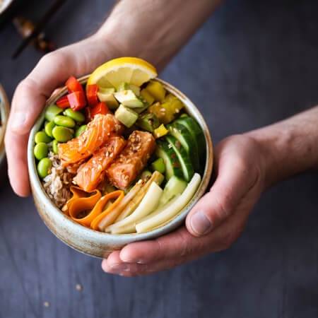 Une personne tenant un bol de nourriture contenant des légumes et du saumon.