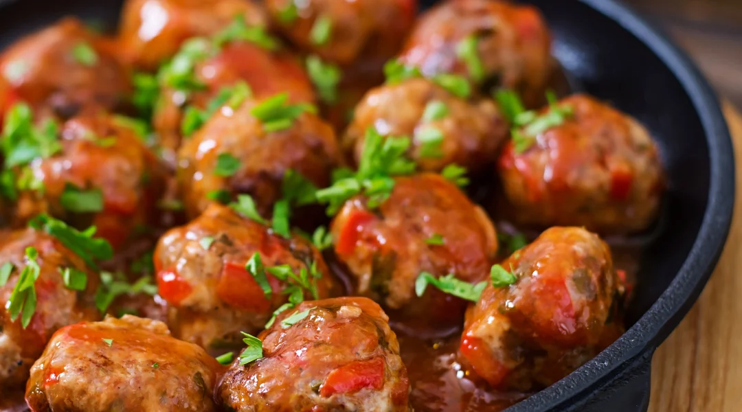 Boulettes de viande dans une sauce, cuites dans une poêle sur une table en bois, évoquant un repas de Noël simple.